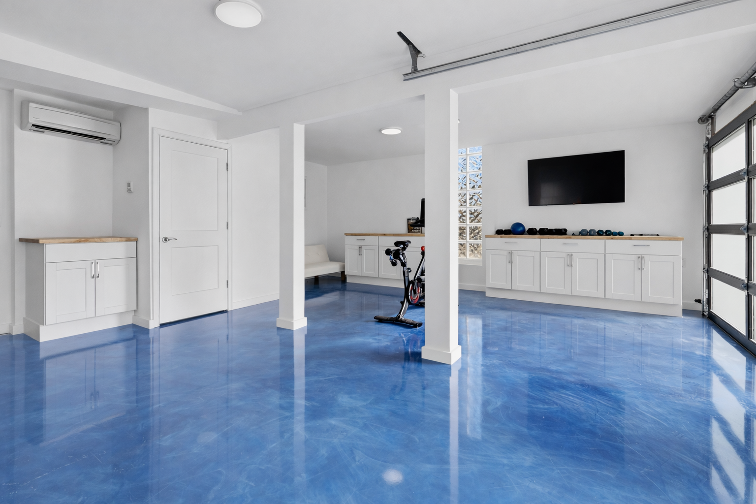 Finished garage and fitness space with blue epoxy floors and custom white cabinetry