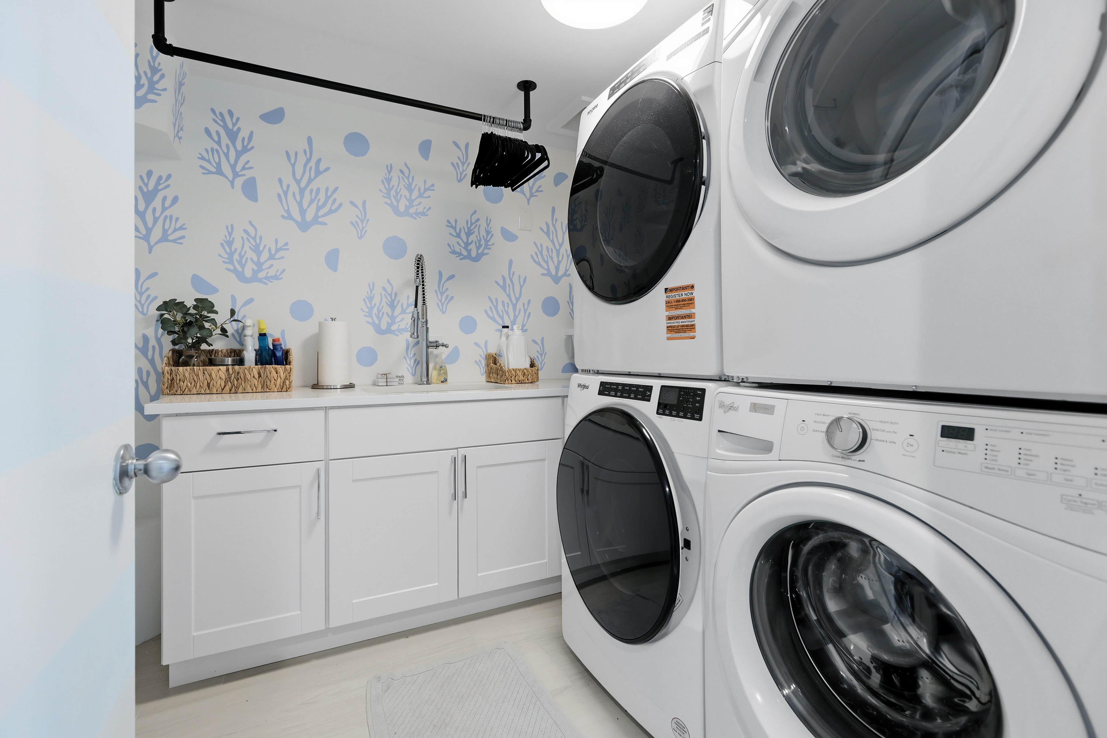 Laundry room with dual washer/dryer units, white cabinetry, and coastal wallpaper