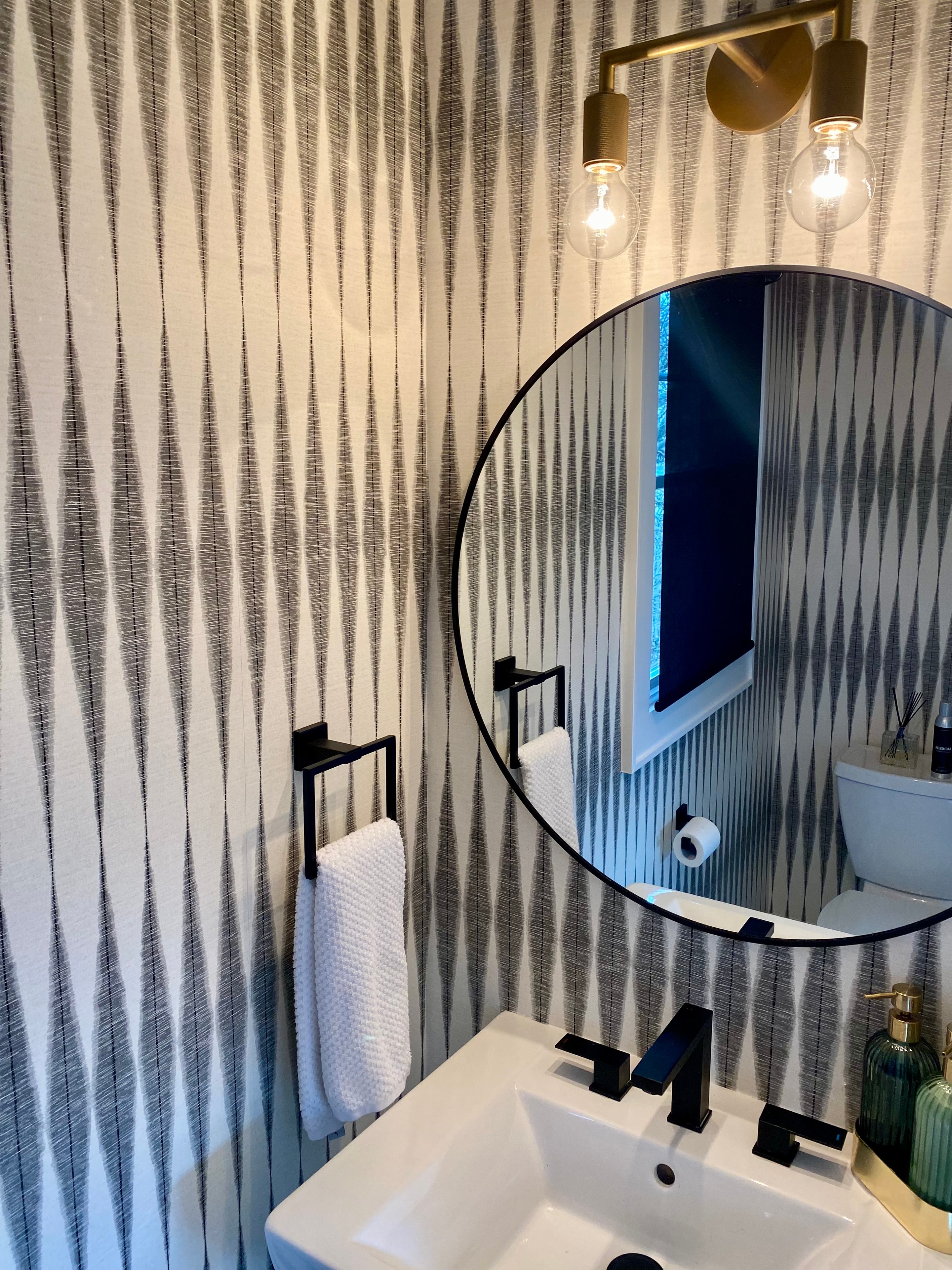 Renovated powder room with bold wallpaper, round mirror, and matte black fixtures
